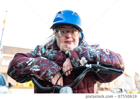 Outdoor portrait of a 39 year old white woman with the Down Syndrome wearing a blue bike helmet 87550619