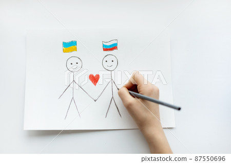 A child draws on a piece of paper two children with a drawing of two flags of Ukraine and Russia close-up. View from above. Children against war A child draws on a piece of paper two children with a drawing of two flags of Ukraine and Russia close-up. View from above. Children against war 87550696