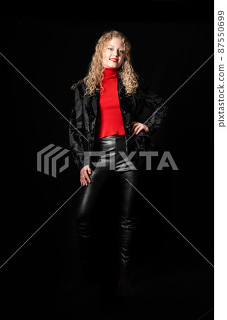 Studio Portrait of a 21 year old white blonde woman with curling hair, full length, wearing leather pants 87550699