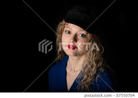 Studio portrait of a 21 year old white blonde woman with curling hair wearing a hat 87550704
