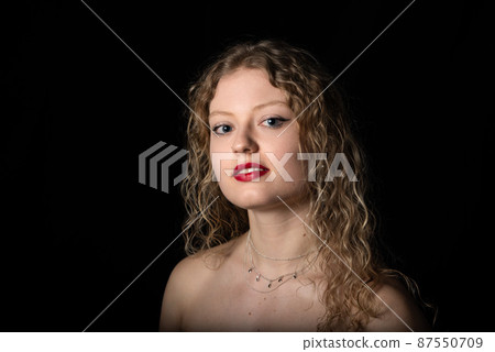 Studio Portrait of a 21 year old white blonde woman with curling hair, naked shoulders Studio Portrait of a 21 year old white blonde woman with curling hair, naked shoulders 87550709