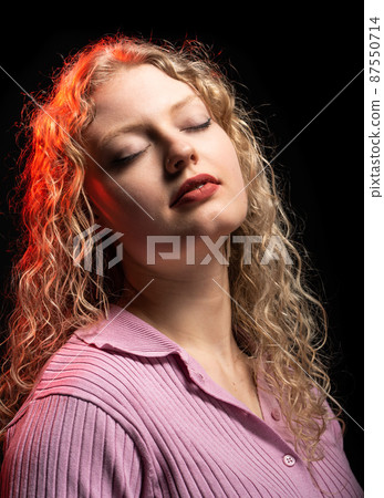 Studio Portrait of a 21 year old white blonde woman with curling hair, eyes closed Studio Portrait of a 21 year old white blonde woman with curling hair, eyes closed 87550714