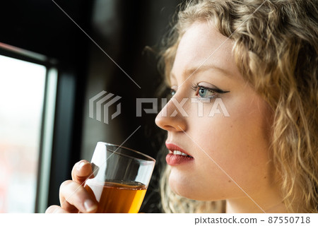 Window portrait of a 21 year old white blonde woman with curling hair holding a glass of champaign Window portrait of a 21 year old white blonde woman with curling hair holding a glass of champaign 87550718