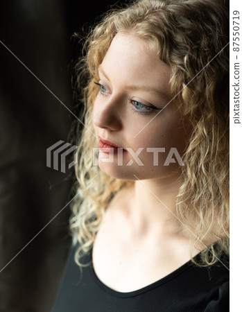 Window portrait of a 21 year old white blonde woman with curling hair Window portrait of a 21 year old white blonde woman with curling hair 87550719
