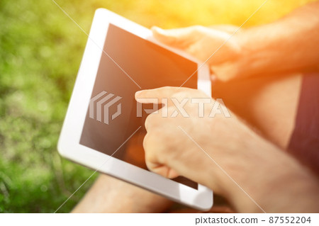 Young hipster boy sitting in the park and using modern digital tablet Young hipster boy sitting in the park and using modern digital tablet 87552204