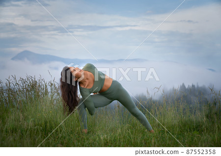 Athletic young woman in sport clothes practising yoga with amazing view on mountains. Concept of strength, motivation and wellbeing. 87552358
