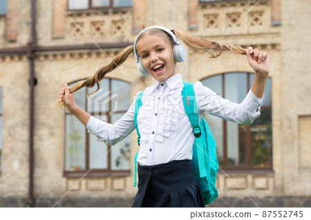 Happy school girl in uniform having fun listening to music in headphones and holding hair Happy school girl in uniform having fun listening to music in headphones and holding hair 87552745