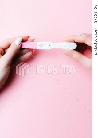 Pregnancy test couple. Positive woman pregnant test in hands with pink silk ribbon on pink background. New life and new family. Motherhood, pregnancy, birth control concept. 87553456