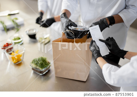 Cooks prepare take away food and packing them into paper bag for delivery 87553901