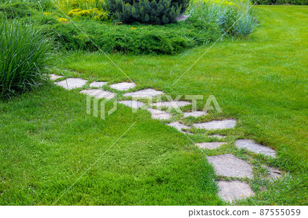 rough different shapes of natural stone path paved in the green backyard turf lawn, crescent backyard walkway landscape with bushes, nobody. rough different shapes of natural stone path paved in the green backyard turf lawn, crescent backyard walkway landscape with bushes, nobody. 87555059