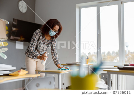 Teacher disinfecting tables in school during coronavirus epidemic 87556011
