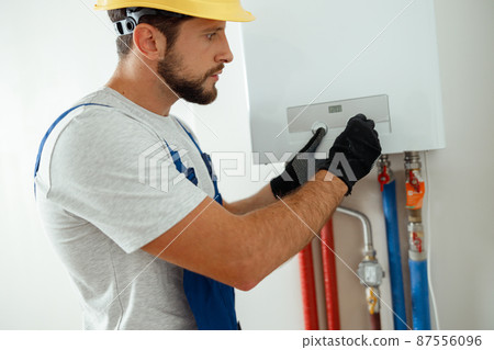 Serious technician setting the new gas boiler for hot water and heating 87556096
