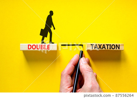 Double taxation symbol. Concept words Double taxation on wooden blocks on a beautiful yellow table yellow background. Businessman hand. Business tax and double taxation concept, copy space. 87556264