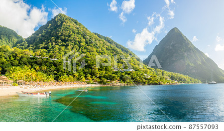 Caribbean beach with palms and straw umrellas on the shore with Gros Piton mountain in the background, Sugar beach, Saint Lucia Caribbean beach with palms and straw umrellas on the shore with Gros Piton mountain in the background, Sugar beach, Saint Lucia 87557093
