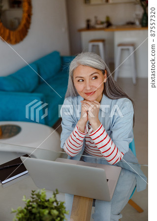 Joyful woman sitting at the table with laptop at home 87557320