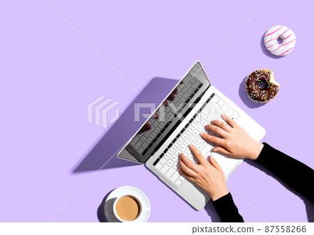 Person using a laptop computer with a donut and a cup of coffee 87558266