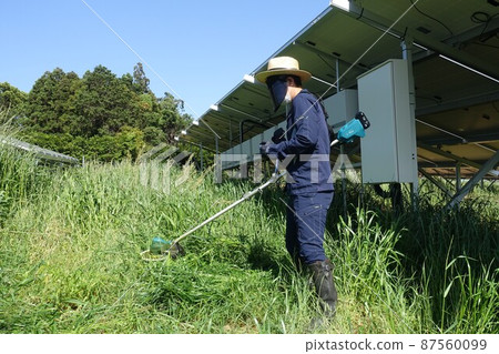 Weeding work at a solar power plant, a man mowing grass Weeding work at a solar power plant, a man mowing grass 87560099