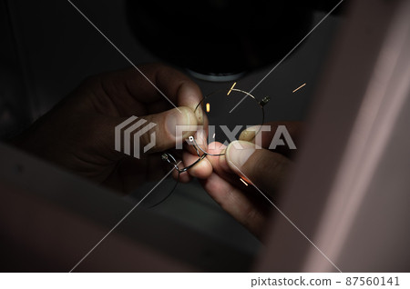 The technician solders the metal frame of the glasses. 87560141