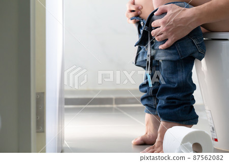 Man sitting on toilet with toilet paper in restroom, Constipation and Hemorrhoids concept 87562082