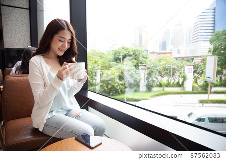 Beautiful Asian woman holding coffee cup in the cafe nearing the window glass 87562083