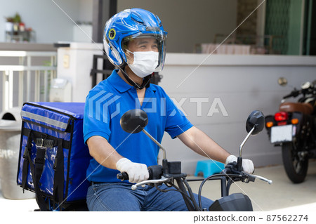 Delivery man wearing blue uniform riding motorcycle and delivery box. Motorbike delivering food or parcel express service Delivery man wearing blue uniform riding motorcycle and delivery box. Motorbike delivering food or parcel express service 87562274