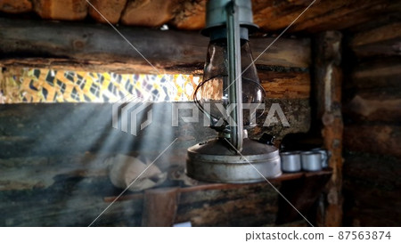 A wooden dugout in which a kerosene lamp burns. Light from the window penetrates into the room. A wooden dugout in which a kerosene lamp burns. Light from the window penetrates into the room. 87563874