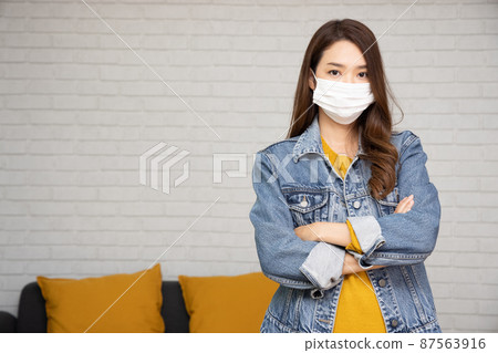 Portrait of Asian women wearing protective medical mask for prevent virus Covid-19 and arms crossed in the living room at home 87563916