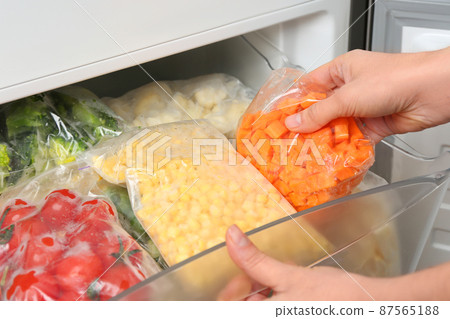 Woman putting plastic bag with carrot in refrigerator with frozen vegetables, closeup 87565188