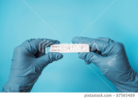 Doctor hand holding negative rapid lateral flow COVID 19 tests over bright blue color background 87565489