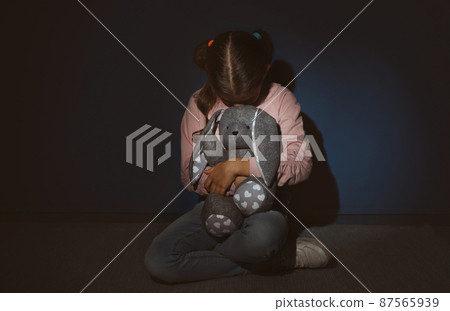 Scared little girl with toy near blue wall. Domestic violence concept Scared little girl with toy near blue wall. Domestic violence concept 87565939