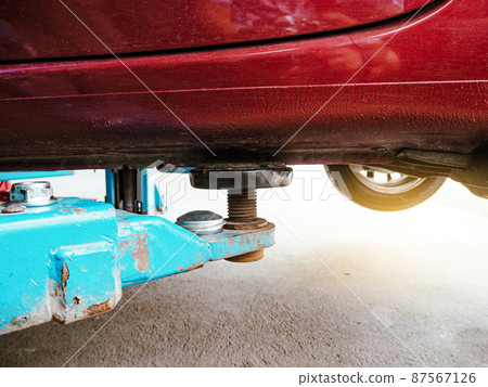Vehicle hydraulic floor jack raises the car body for repairs in an auto repair garage Vehicle hydraulic floor jack raises the car body for repairs in an auto repair garage 87567126