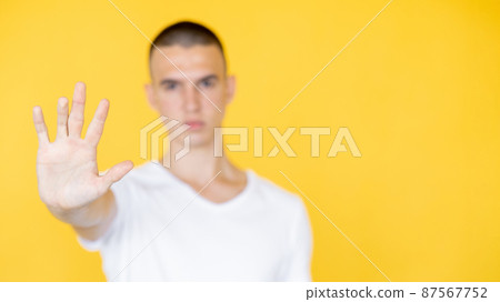 Protesting gesture. Defocused man. Stop do it. Strict guy holding forbidden hand up expressing confident emotion isolated yellow copy space. Protesting gesture. Defocused man. Stop do it. Strict guy holding forbidden hand up expressing confident emotion isolated yellow copy space. 87567752
