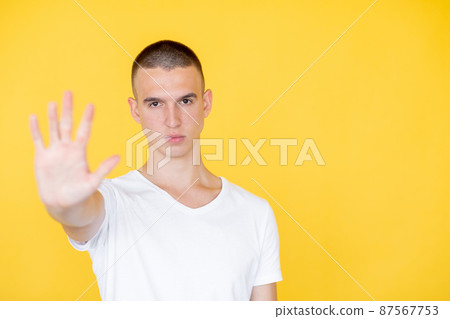 Stop gesture. Strict man. Closed way. Serious gloomy defocused guy in t-shirt holding forbidden hand up expressing protest isolated yellow copy space. 87567753