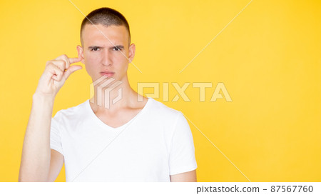 Small size. Serious man. Measurement gesture. Concentrated handsome guy showing fingers sign of little bit isolated yellow copy space. 87567760