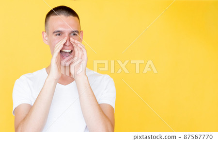 Megaphone gesture. Shouting man. Important information. Happy smiling guy holding hands on mouth like horn isolated yellow copy space. 87567770
