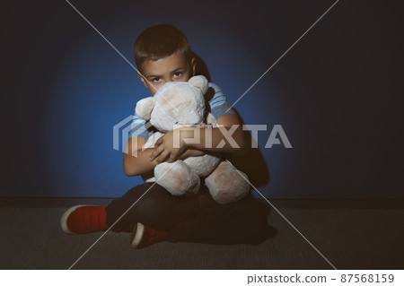 Sad little boy with teddy bear near blue wall. Domestic violence concept 87568159