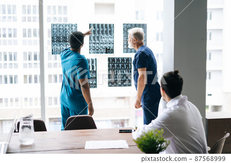 Group of multi-ethnic skilled doctors discussing together history disease of patient using MRI scan during medical conference standing near window. Concept of modern medicine and health care. Group of multi-ethnic skilled doctors discussing together history disease of patient using MRI scan during medical conference standing near window. Concept of modern medicine and health care. 87568999