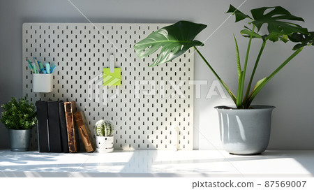 Home office desk with potted plants, books and pegboard on white table in home office. Home office desk with potted plants, books and pegboard on white table in home office. 87569007