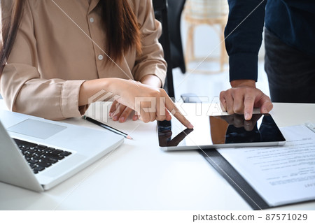 Two young business partners using digital tablet and discussing plans or ideas at meeting room. Two young business partners using digital tablet and discussing plans or ideas at meeting room. 87571029