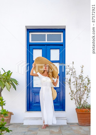 A beautiful tourist wearing straw hat standing over blue door at the balcony A beautiful tourist wearing straw hat standing over blue door at the balcony 87572921