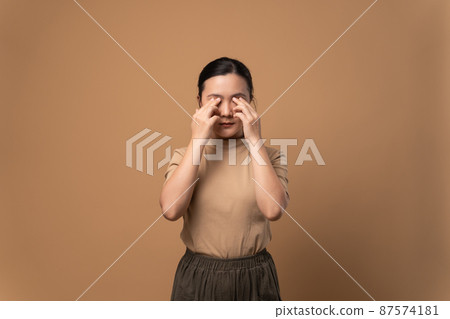 Asian woman was sick with eyes pain standing isolated on beige background. Asian woman was sick with eyes pain standing isolated on beige background. 87574181
