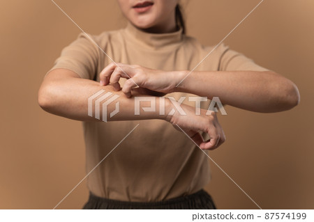 Asian woman was sick with irritate itching her skin standing isolated on beige background. Asian woman was sick with irritate itching her skin standing isolated on beige background. 87574199