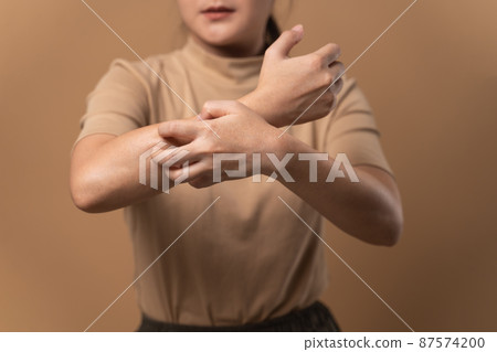 Asian woman was sick with irritate itching her skin standing isolated on beige background. 87574200