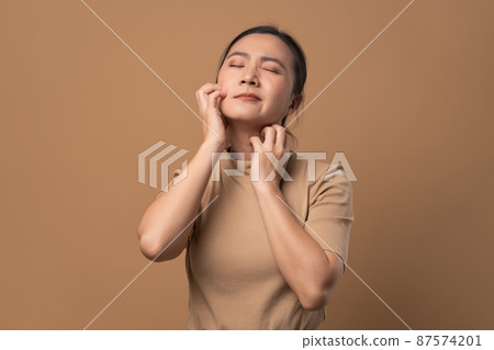 Asian woman was sick with irritate itching her skin standing isolated on beige background. 87574201