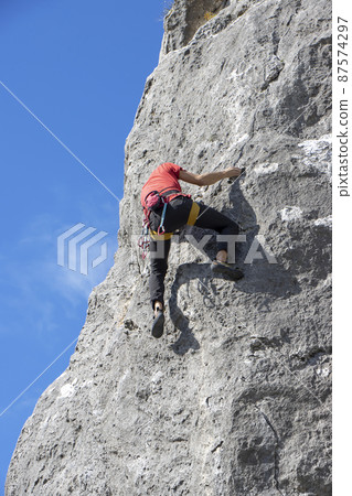 Young male climber climbs on a cliff Young male climber climbs on a cliff 87574297