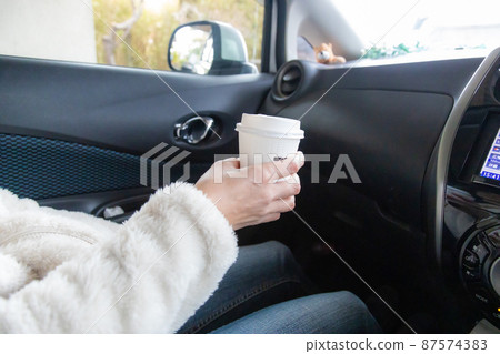 A woman drinking coffee in a duo in the car 87574383