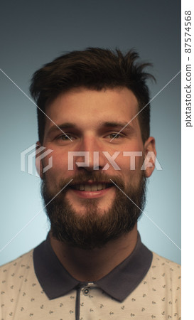 Portrait of smiling bearded young male model rejoices coming weekends, dressed casually, over blue background. Happy face smiling looking at the camera Portrait of smiling bearded young male model rejoices coming weekends, dressed casually, over blue background. Happy face smiling looking at the camera 87574568