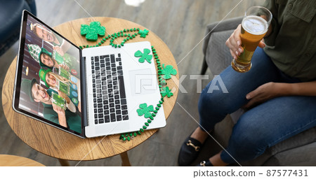 Caucasian woman holding beer at bar making st patrick's day video call to friends on laptop Caucasian woman holding beer at bar making st patrick's day video call to friends on laptop 87577431