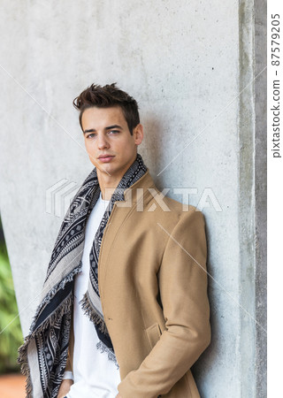 Portrait of stylish handsome young man standing outdoors and leaning on wall. Man wearing jacket and scarf Portrait of stylish handsome young man standing outdoors and leaning on wall. Man wearing jacket and scarf 87579205