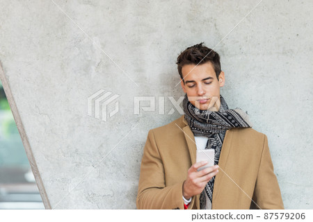 Businessman texting on mobile phone against wall Businessman texting on mobile phone against wall 87579206